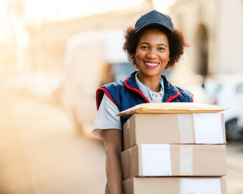 Portrait of happy black courier delivering packages and looking at the camera.