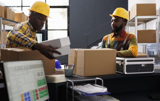 Warehouse employees putting packed boxes on counter desk ready for shipment. African american e commerce retail storehouse managers preparing customer packages for transportation